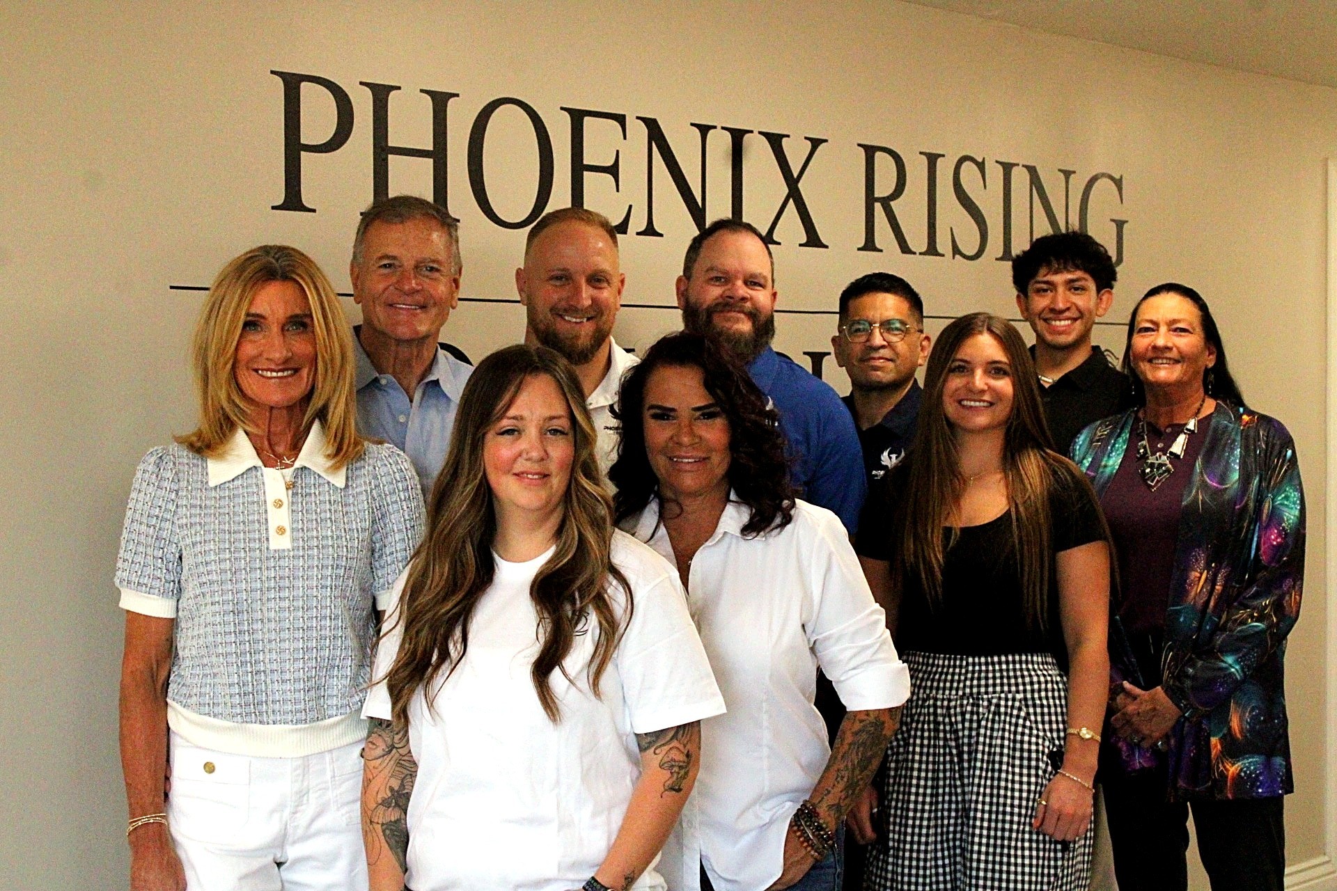 The Phoenix Rising team standing together in front of the Phoenix Rising wall